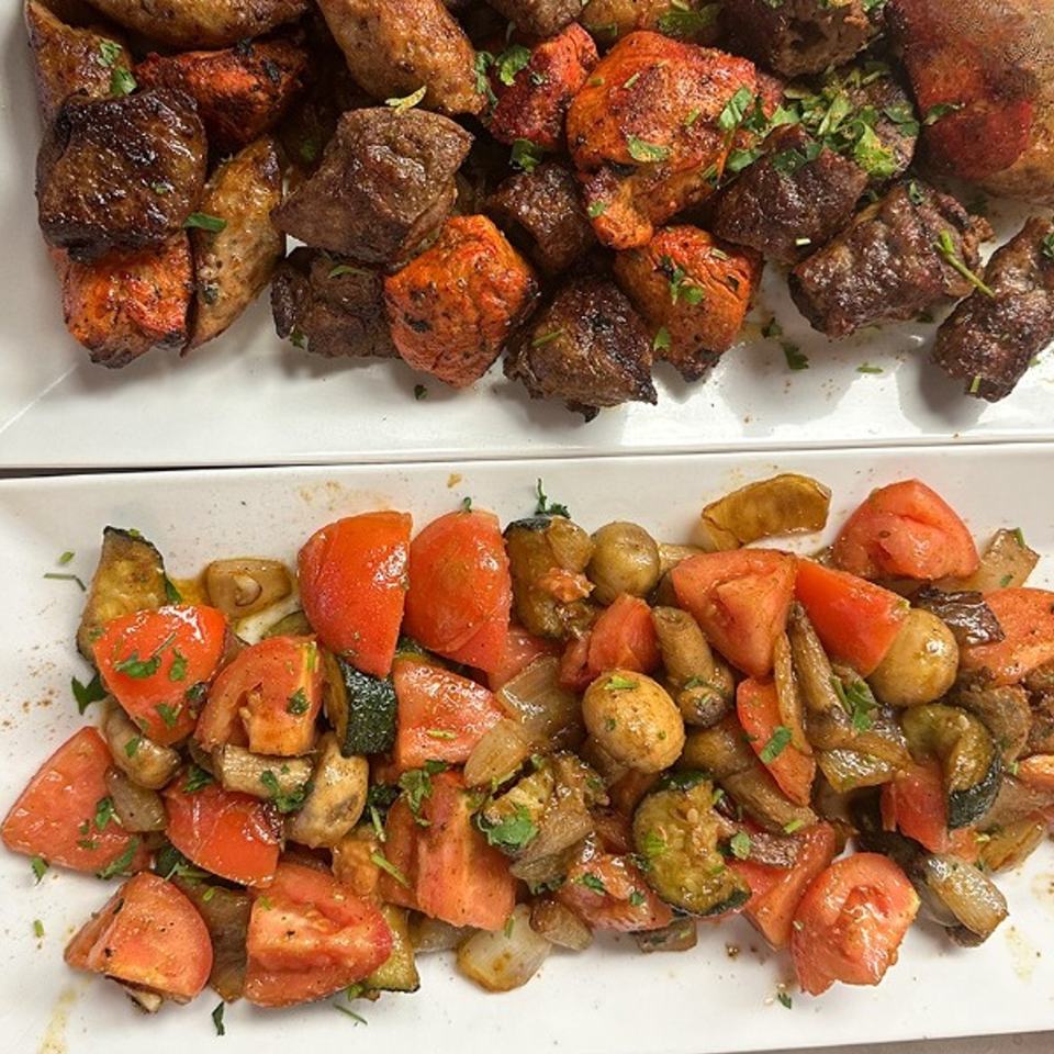 Plates of grilled Mediterranean chicken and beef with roasted vegetables, including tomatoes, zucchini, and mushrooms.