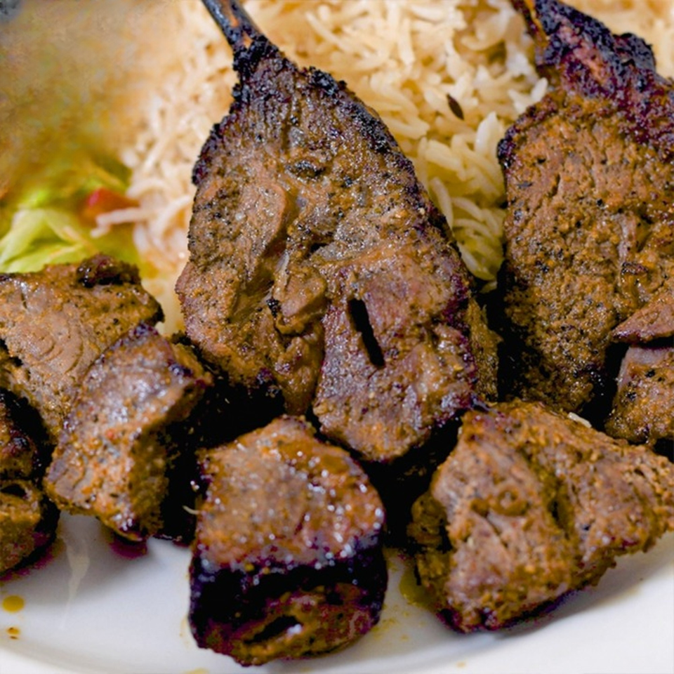 Close-up of grilled meat skewers and cubed meat pieces, served with rice and a side salad.