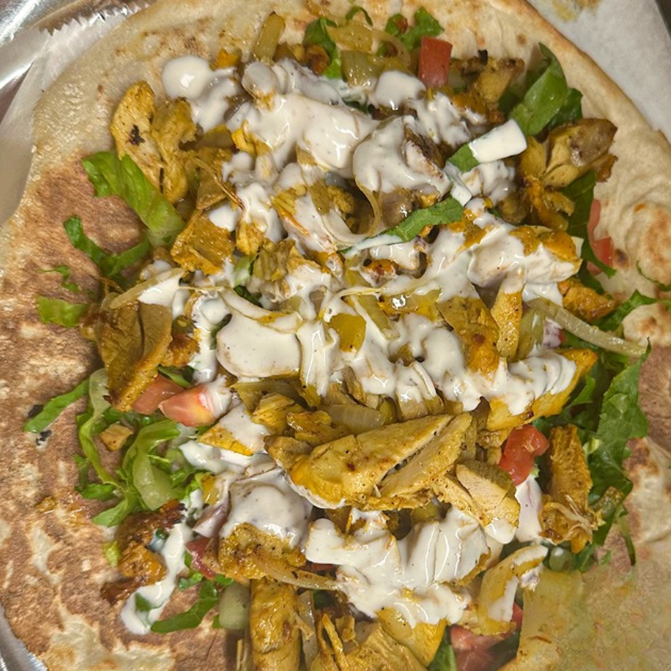 Halal chicken shawarma on flatbread with lettuce, tomatoes, onions, and white sauce.